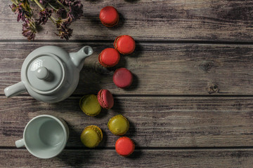 White teapot, cup, bouquet of field flowers and colorful macaroons on the wooden table.