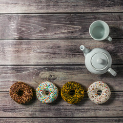 White teapot, cup and colorful donuts on the wooden table. Tea time at sweet home.