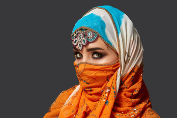 Studio shot of a chrming female wearing the colorful hijab decorated with sequins and jewelry. Arabic style.