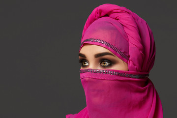 Close-up shot of a young charming woman wearing the pink hijab decorated with sequins. Arabic style.