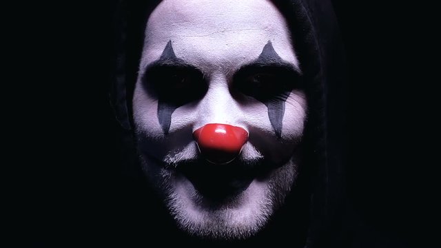 Creepy clown smiling into camera isolated on black background, horror, close-up