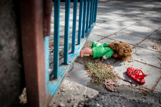 Old doll toy and red sandal thrown on the ground by the blue gate.