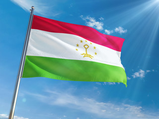 Fototapeta na wymiar Tajikistan National Flag Waving on pole against sunny blue sky background. High Definition