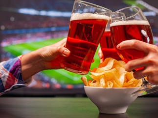 Happy friends or football fans are clinking glasses of beer