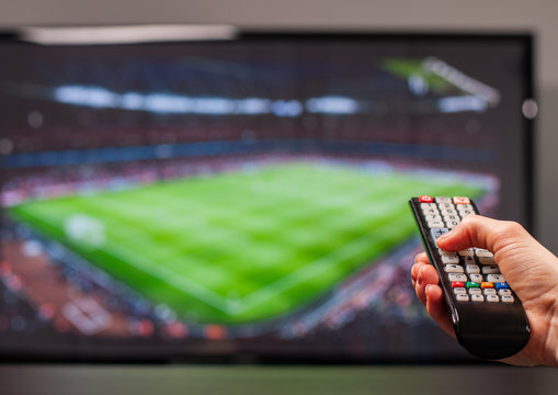 Man watching football match on television, the remote control in hand.