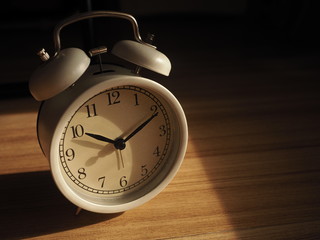 White analog clock and shadow on wooden floor and sunlight from window shine on the clock