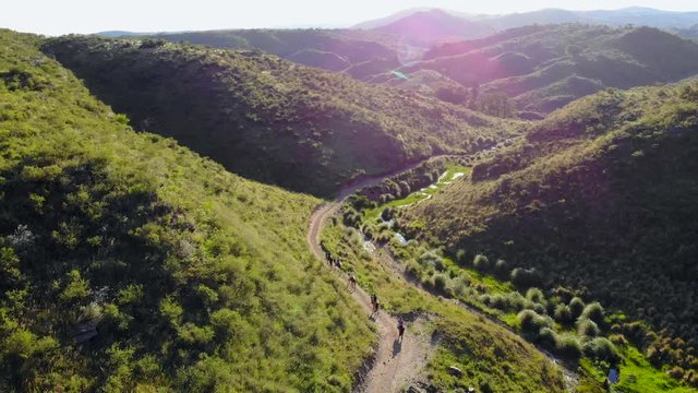 Aerial 4k drone shot, panning around a group of people horseback riding through a journey, between green hills, on a sunny day, in Cordobas fields, Argentina