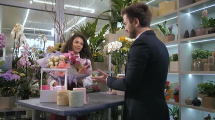 Cheerful attractive female floral artist giving gorgeous flower arrangement to satisfied customer with good wishes. Happy woman with pleasure listening to praise of her floral creation in flower shop