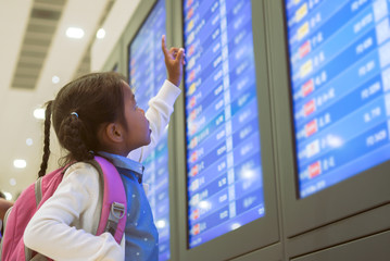 Cute asian child girl with backpack checking her flight at information board in international...