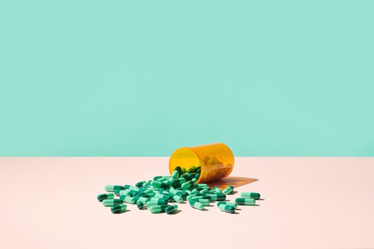 Colorful Prescription Pills Spilling Out of RX Medicine Bottle on Pale Pink Surface  with blue green background. 