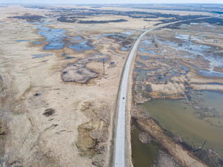 Aerial view of a marshland near a highway with an asphalt road during a spring flood, which floods and blurs the road under a clear blue sky without clouds. Natural disasters of the environment.