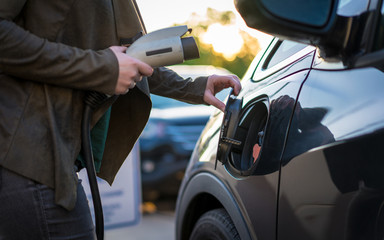 Young woman plug in charging electric vehicle downtown Fayetteville Arkansas, holding power charger...