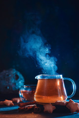 Glass teapot with rising steam and star-shaped cookies on a dark background with copy space. Astronomy themed