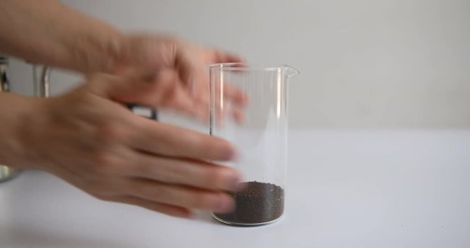 Pouring ground coffee and water in french press glass to make cold brew coffee