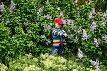Fototapeta na wymiar Cute boy in spring garden with blooming lilac . Children's walks in the fresh air