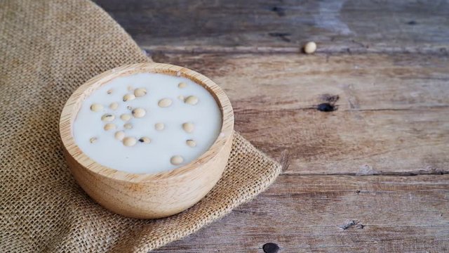 Video footage of fresh raw soybeans pouring into soy milk in wooden bowl with soy bean on gunny sack cloth, copy space, full high defination resolution, 29.97 frame per second, slowmotion