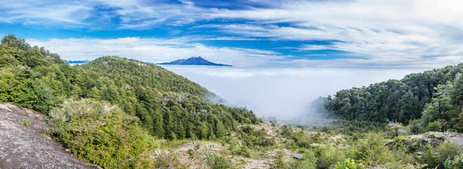 Fototapeta na wymiar Amazing panoramic view from Osorno Volcano to an awe sea of clouds scenery on an amazing forest with Patagonia mountain range on the far distance. An awe wilderness scenery on a remote location