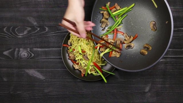 Stir fryed noodls with garlic sprouts and chopped pieces of mushrooms with chicken laid out on a plate with a wok frying pan. Cooking with champignons and fried noodles according to homemade recipe.