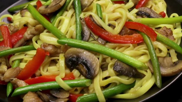 Stir fryed noodls with garlic sprouts and chopped pieces of mushrooms with chicken saut&eacute;ed in an oil in a wok pan. Cooking with champignons and fried noodles according to homemade recipe. Close.