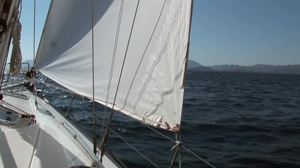 White sails and rope on sailing boat details on deck of moving sailing yacht on background of water surface and blue sky during sea journey. Yachting as an relaxation active lifestyle.