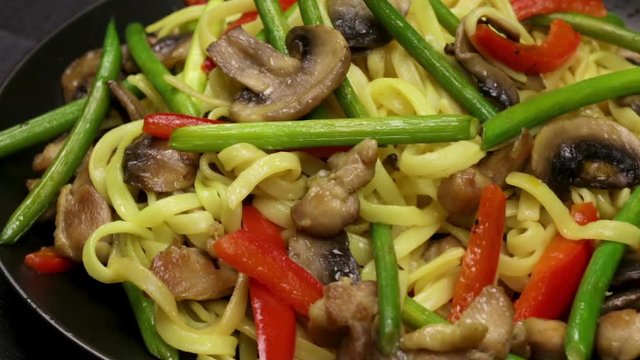 Stir fryed noodls with garlic sprouts and chopped pieces of mushrooms with chicken saut&eacute;ed in an oil in a wok pan. Cooking with champignons and fried noodles according to homemade recipe. Close.