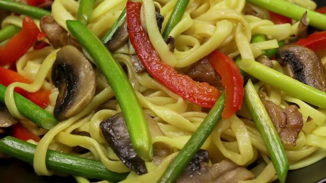 Stir fryed noodls with garlic sprouts and chopped pieces of mushrooms with chicken saut&eacute;ed in an oil in a wok pan. Cooking with champignons and fried noodles according to homemade recipe. Close.