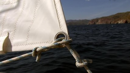 Details and rope close-up of white sails on deck of moving sailing yacht on background of water surface and blue sky during sea journey. Yachting as an relaxation active lifestyle.