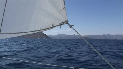 Details and rope close-up of white sails on deck of moving sailing yacht on background of water surface and blue sky during sea journey. Yachting as an relaxation active lifestyle.