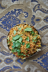 Top view of Bhelpuri in a bowl, a popular Indian street food made of puffed rice, vegetables, potatoes, mango, cilantro, peanuts, spices with green and tamarind chutneys.