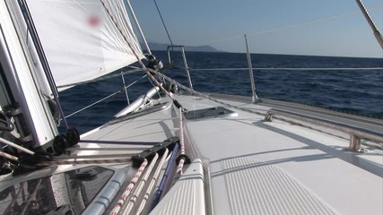 White sails and rope on sailing boat details on deck of moving sailing yacht on background of water surface and blue sky during sea journey. Yachting as an relaxation active lifestyle.