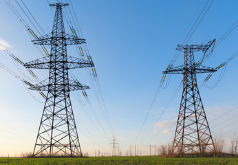High voltage lines and power poles and green agricultural landscape during sunrise.