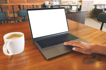 Mockup image of a woman's hand using and touching on laptop touchpad with blank white desktop screen with coffee cup on wooden table