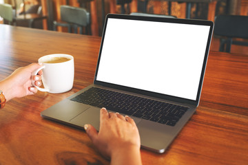 Mockup image of a woman's hand using and touching on laptop touchpad with blank white desktop screen while drinking coffee on wooden table