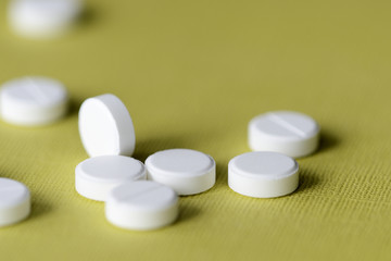 White tablets scattered on a green-yellow background close up