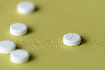 White tablets scattered on a green-yellow background close up