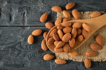 Almonds in a wooden spoon on a piece of burlap on a dark table. Vegetarian food. Flat lay.