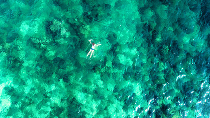 Aerial top view of woman snorkeling from above, girl snorkeler swimming in a clear tropical sea water with corals during summer vacation in Thailand - obrazy, fototapety, plakaty