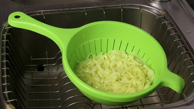 The noodles are laid out in colander after cooking. Hot water flows into the sink with pasta.