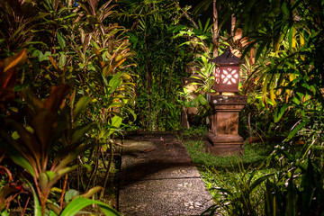 Fototapeta na wymiar Decorative lamp on the stone pillar next to the path in the tropical garden at night . Island Bali, Indonesia . Nature concept