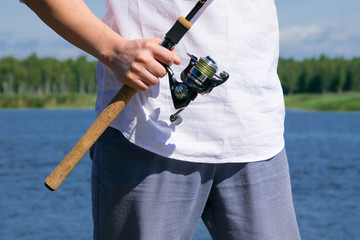the hand of the fisherman holding the rod in the open air, in front of a white shirt