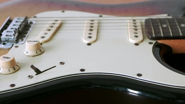 Slide motion of old electric guitar with a fine pattern of guitar strings placed on a wooden floor table