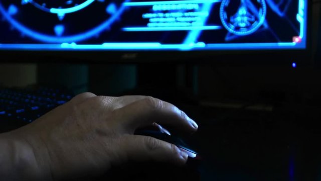 Close up of a hacker's hand using a computer mouse, hi-tech screen in the background