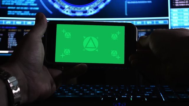 Hackers hands using a smartphone (landscape) in front of hi-tech screens, green screen for replacement