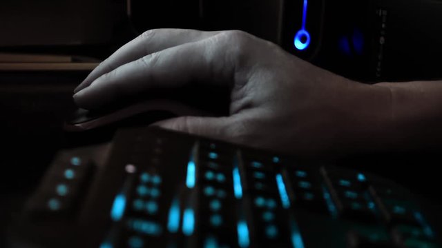 Close up on the hand of a hacker using a computer mouse, dark office
