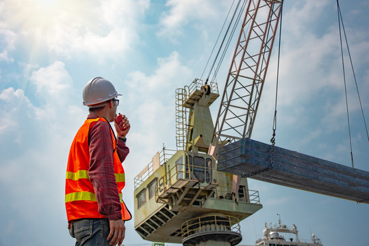worker stevedore foreman, engineering, loading master talks to crane driver by walkie talkie for safety lifting the goods shipment, lifting by gantry crane, working at risk on the high level insurance