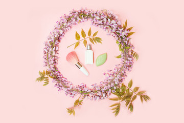 Circle frame of cosmetics makeup, green soap and beautiful wisteria flowers branch with blossoms buds on pink background.