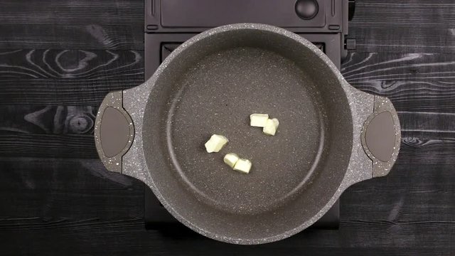 Female's chef hands put butter in a frying pan. Pieces of oil melt and spread on the hot surface of the bottom. Part of the process of cooking on the homemade recipe.