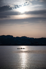 three people in a canoe with the sunset in the middle of the sea