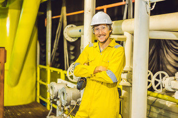 Young man in a yellow work uniform, glasses and helmet in industrial environment,oil Platform or...