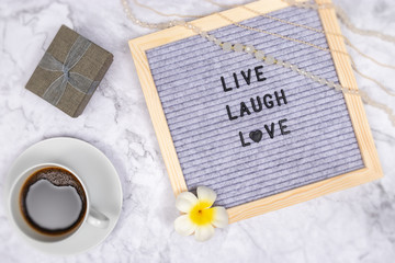 word live laugh love on letter board on white marble desk background with coffee cup and gift box , decoration with flower and luxury pink necklace